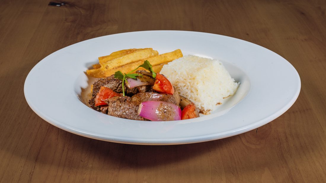 Lomo Saltado — stir-fried sirloin with red onion, tomato, fries and rice.